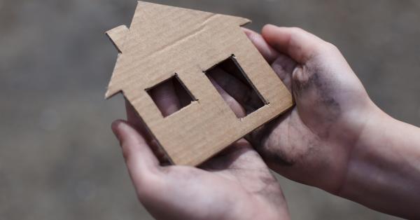 Et par barnehænder holder et stykke pap, der er skåret ud som et hus.