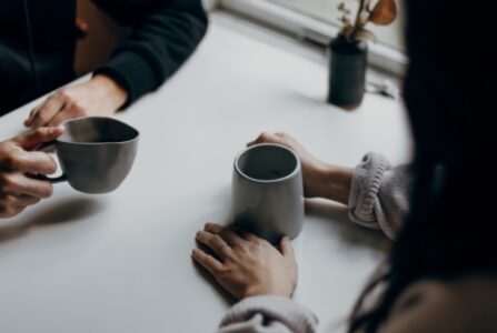 To mennesker sidder ved et bord, med hænderne om kaffekrus.