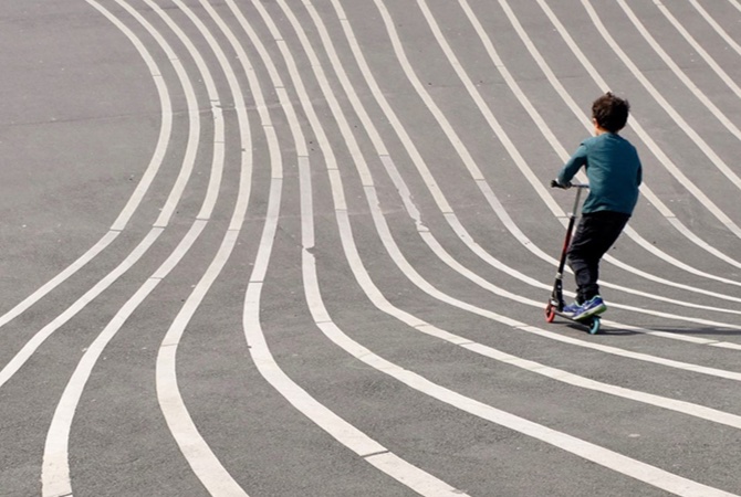 Barn på løbehjul på en stribet, asfalteret bakke.